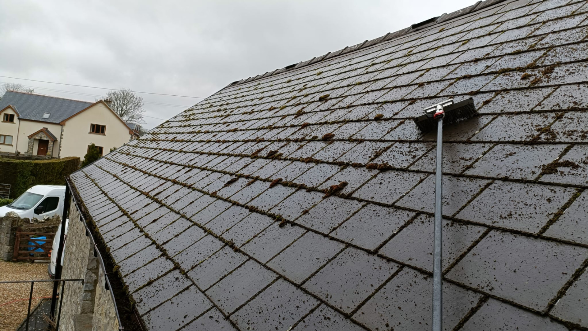 Before: slate roof covered in moss and debris, being scrubbed with a long-reach brush